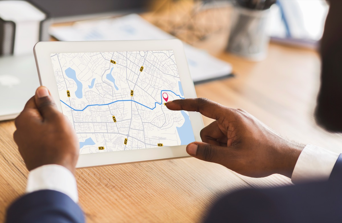 A person holding a tablet that shows a city map with a route and a red location pin